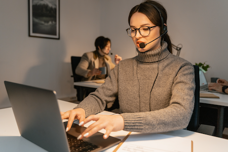 woman with glasses wearing headset with microphone while typing on computer