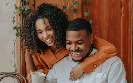 Woman in orange shirt leaning down over man's shoulder, both looking at something out of the frame